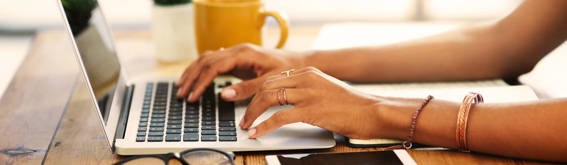 E-learning tanfolyamok – laptopon gépelő kezek egy faasztalnál, mellettük bögre kávé